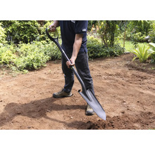 Muž drží rýč v zahradě.