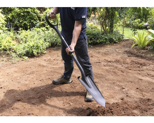 Muž drží rýč v zahradě.