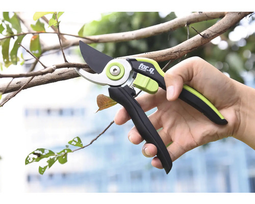 Osoba drží zahradnické nůžky značky for_q při prořezávání větve.