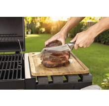 Připravený steak se krájí nožem na dřevěném prkénku vedle grilu.
