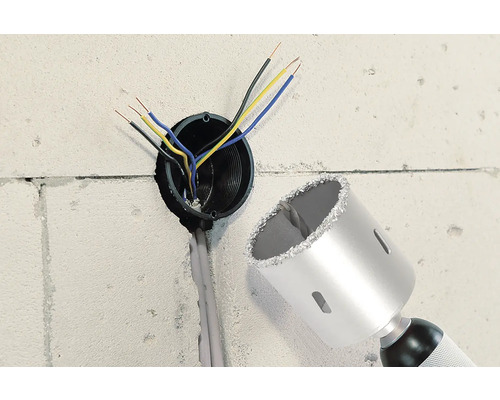 Stěna s vyvrtaným otvorem, elektrickými kabely a korunkovým vrtákem.