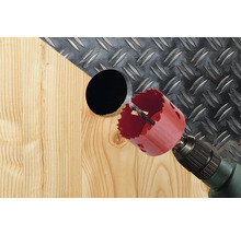 Děrovací pila vrtá otvor do dřeva s rýhovaným plechem v pozadí