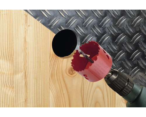 Děrovací pila vrtá otvor do dřeva s rýhovaným plechem v pozadí