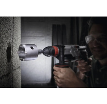 Vrtací stroj s děrovkou vrtá otvor do betonové zdi.