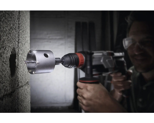 Vrtací stroj s děrovkou vrtá otvor do betonové zdi.