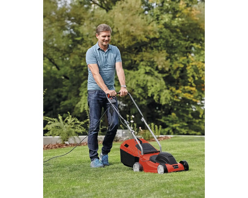Muž seče trávník elektrickou sekačkou.