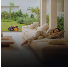 Žena odpočívá na gauči, zatímco robotická sekačka seká trávník