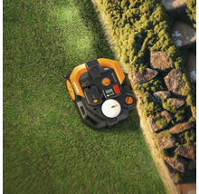 Pohled shora na robotickou sekačku na trávníku u kamenné zdi.