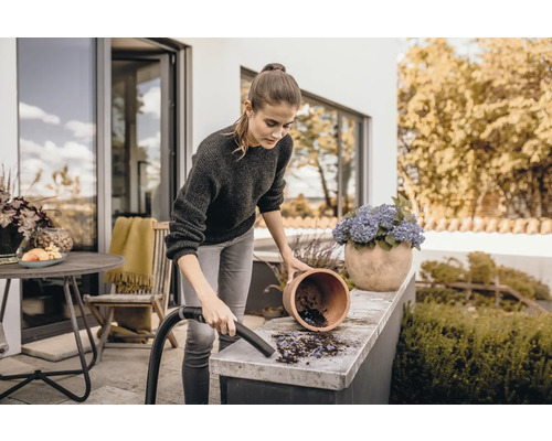 Žena čistí terasu vysavačem vedle květináče