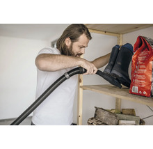 Muž vysává polici s gumáky a pytlem