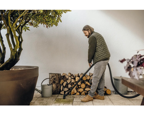 Muž čistí terasu vysavačem popela, v pozadí hromada dřeva a rostlina