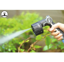 Ruka drží stříkací pistoli zahradní hadice při zalévání rostlin