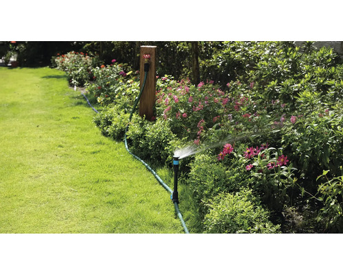 Zavlažování zahrady pomocí zavlažovače trávníku v kvetoucí zahradě.