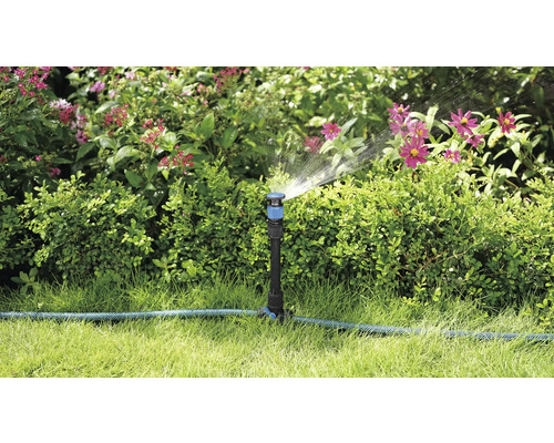 Zahradní scéna se zavlažovačem trávníku, který zavlažuje rostliny
