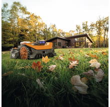 Robotická sekačka na trávníku s listím před obytným domem.