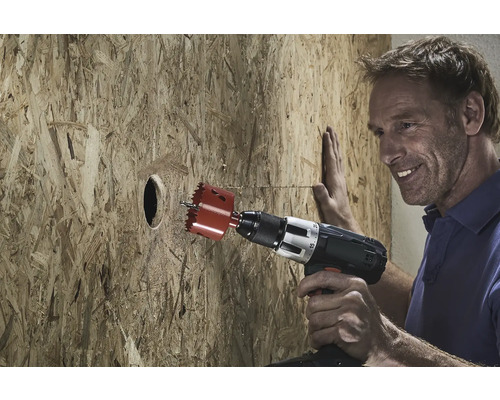 Muž vrtá díru do dřevěné desky pomocí děrovací pily.