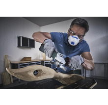 Uživatel s respirátorem, ochrannými brýlemi a rukavicemi opracovává dřevo úhlovou bruskou