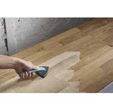 Osoba nanáší povrchovou úpravu trojúhelníkovým štětcem na dřevěnou desku.