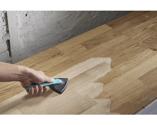 Osoba nanáší povrchovou úpravu trojúhelníkovým štětcem na dřevěnou desku.