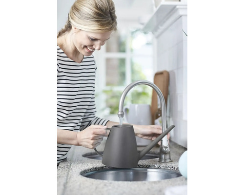 Žena plní šedou konev u vodovodního kohoutku