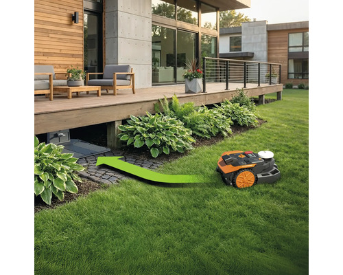 Robotická sekačka s zelenou šipkou jedoucí k nabíjecí stanici pod dřevěnou terasou