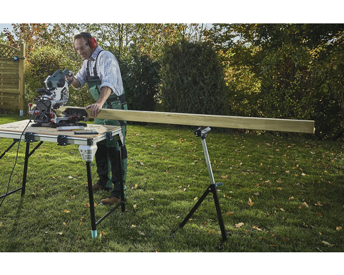 Řemeslník řeže dřevo pokosovou pilou na řezacím stole na zahradě.