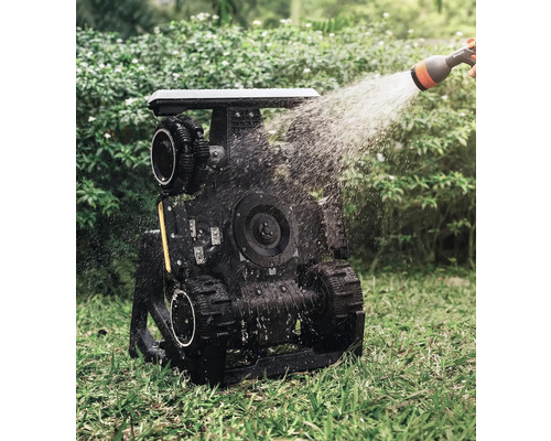 Zavlažovaný zahradní robot s pásovým pohonem v provozu na trávníku.