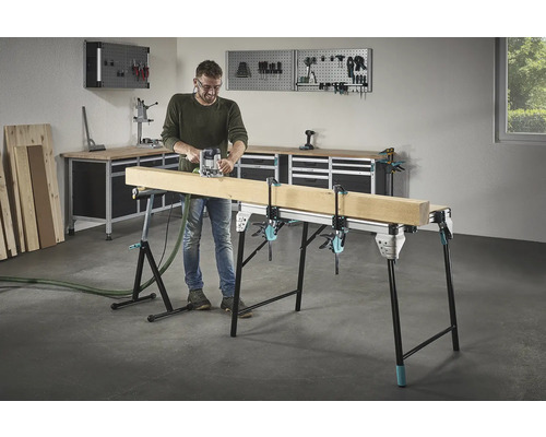 Muž frézuje dřevo na pracovním stole se šroubovými svorkami v dílně