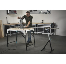 Muž pracuje s vrtačkou na pracovním stole, v pozadí nářadí a pracovní stůl.