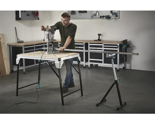 Muž pracuje s vrtačkou na pracovním stole, v pozadí nářadí a pracovní stůl.