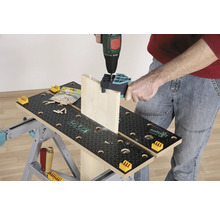 Osoba vrtá dřevěnou desku vrtačkou na pracovní lavici.