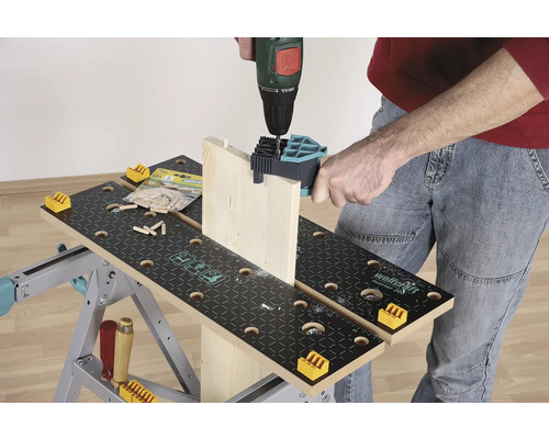 Osoba vrtá dřevěnou desku vrtačkou na pracovní lavici.