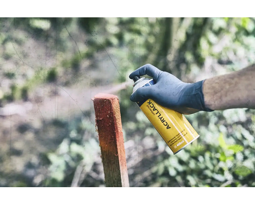 Osoba stříká dřevěný sloupek žlutým univerzálním sprejem