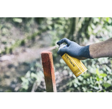 Osoba stříká dřevěný sloupek žlutým univerzálním sprejem