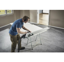 Řemeslník řeže dveře ruční okružní pilou na pracovním stole.