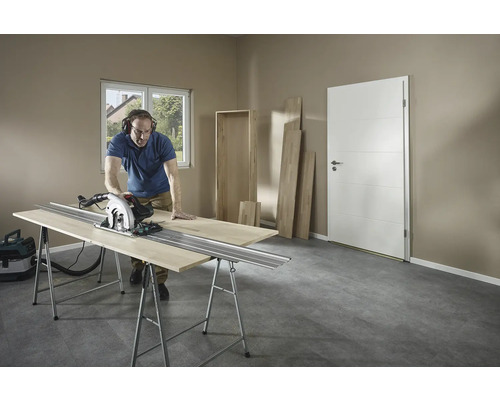 Muž řeže dřevo ruční kotoučovou pilou na ponku v místnosti.