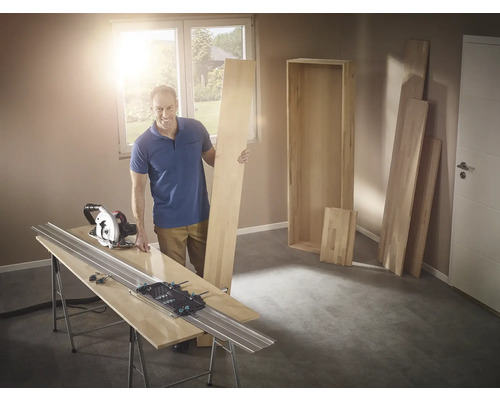 Muž s ruční okružní pilou a vodicí lištou při řezání dřeva na polici