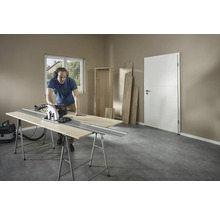 Muž řeže dřevo ruční kotoučovou pilou na ponku v místnosti.