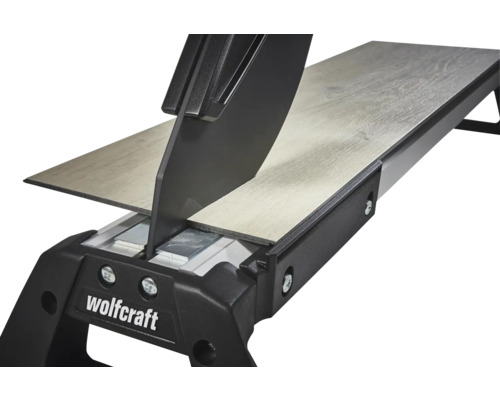 Řezačka na laminát Wolfcraft řeže laminátovou desku s dekorem dřeva. Detailní pohled na řezný mechanismus.