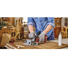 Muž používá lamelovací frézku ke zpracování obrobku. Na stole leží dřevěné destičky a láhev lepidla.