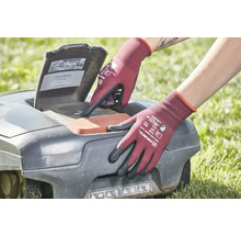 Osoba v zahradních rukavicích obsluhuje robotickou sekačku na trávu.