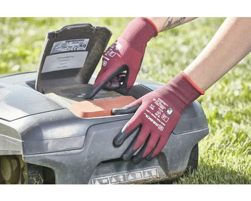 Osoba v zahradních rukavicích obsluhuje robotickou sekačku na trávu.