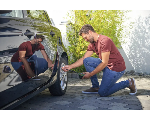 Muž kontroluje tlak v pneumatikách automobilu pomocí měřiče tlaku v pneumatikách.