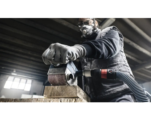 Muž brousí kus dřeva bruskou. Má ochrannou masku a brýle.