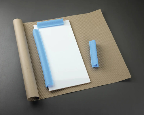 Obalové materiály: skleněná deska, role papíru, vlnitá lepenka a pěnová ochrana.