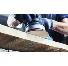 Osoba brousí dřevěnou desku excentrickou bruskou.