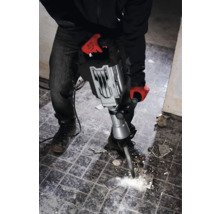 Muž s pracovními rukavicemi používá bourací kladivo k odstranění dlaždic.