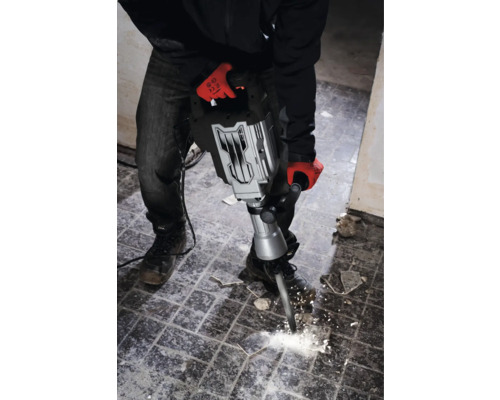 Muž s pracovními rukavicemi používá bourací kladivo k odstranění dlaždic.