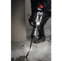 Muž používá bourací kladivo k vytvoření praskliny v betonové podlaze.