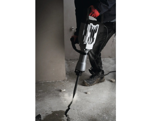 Muž používá bourací kladivo k vytvoření praskliny v betonové podlaze.